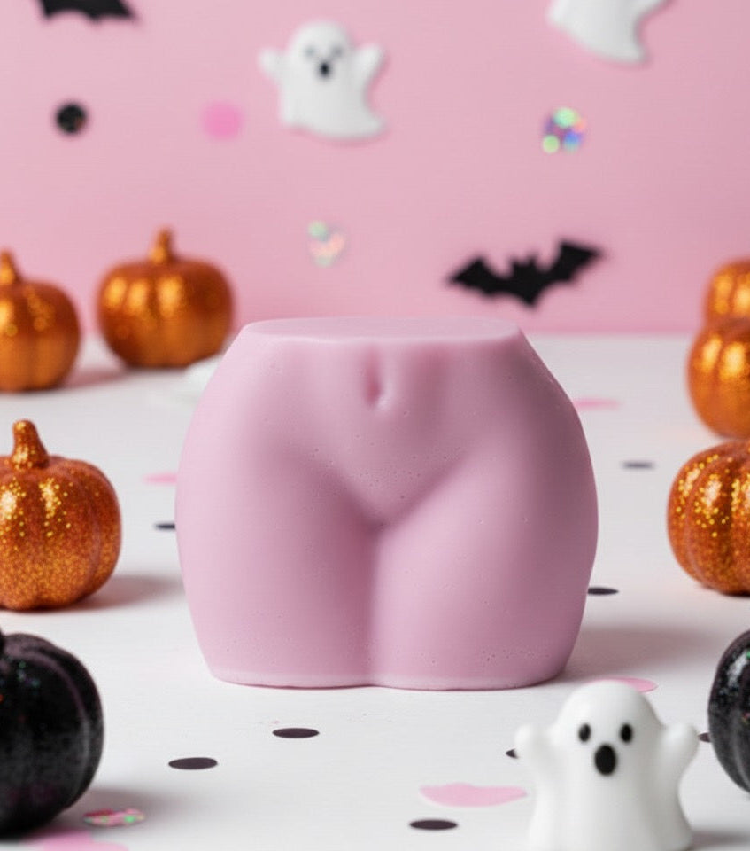 Pink buttocks-shaped candle on a Halloween-themed background with pumpkins and ghosts.