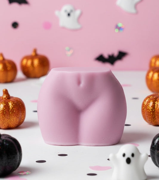 Pink buttocks-shaped candle on a Halloween-themed background with pumpkins and ghosts.